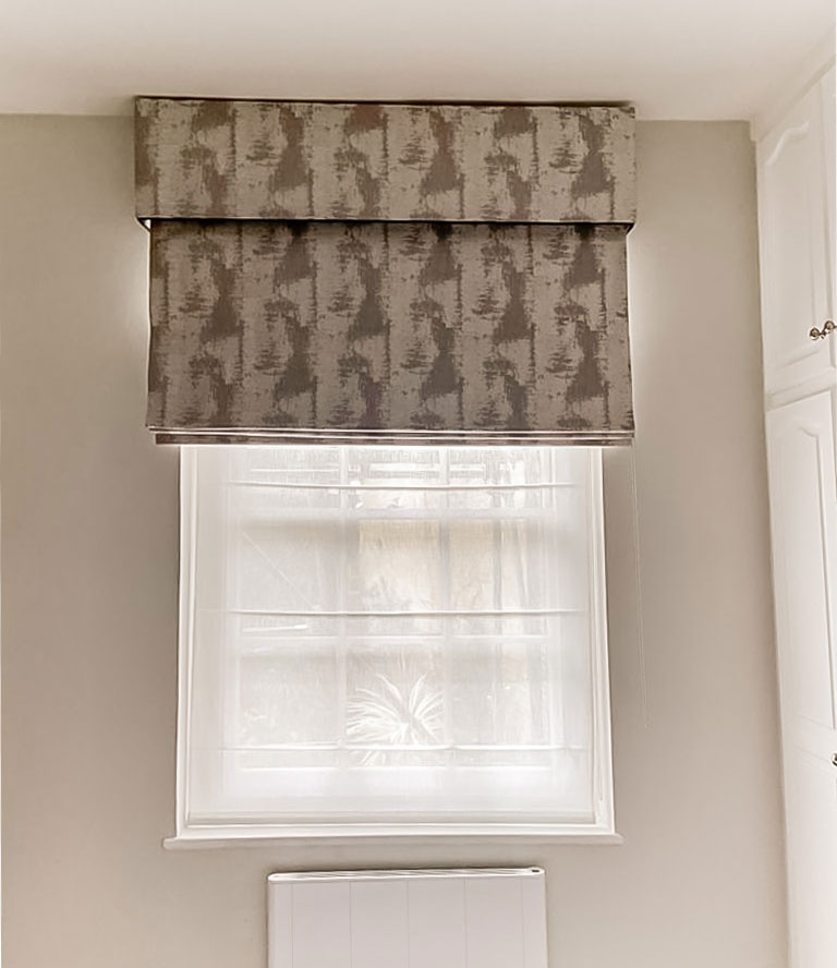A small window with a roman blind in a pelmet